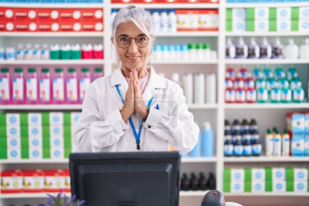 Photo for Middle age woman with tattoos working at pharmacy drugstore praying with hands together asking for forgiveness smiling confident. - Royalty Free Image