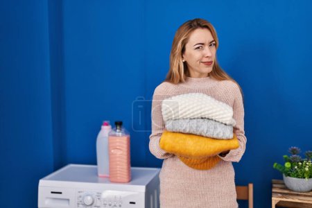 Foto de Hispanic woman holding folded laundry after laundry skeptic and nervous, frowning upset because of problem. negative person. - Imagen libre de derechos