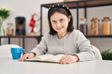 Foto de Mujer joven con síndrome de Down lectura libro sentado en la mesa en casa - Imagen libre de derechos