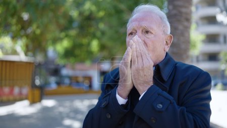 Téléchargez les photos : Senior soufflant de l'air sur les mains pour le froid au parc - en image libre de droit