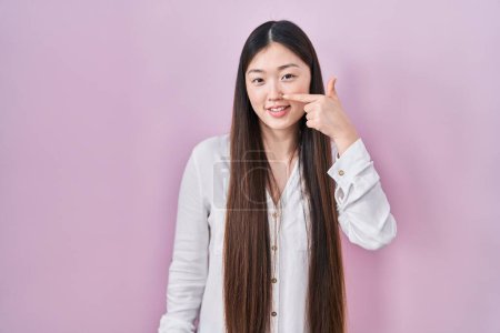 Photo for Chinese young woman standing over pink background pointing with hand finger to face and nose, smiling cheerful. beauty concept - Royalty Free Image
