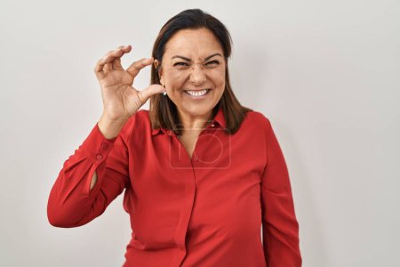 Photo for Hispanic mature woman standing over white background smiling and confident gesturing with hand doing small size sign with fingers looking and the camera. measure concept. - Royalty Free Image