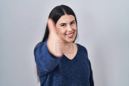 Photo for Young brunette woman standing over isolated background smiling friendly offering handshake as greeting and welcoming. successful business. - Royalty Free Image