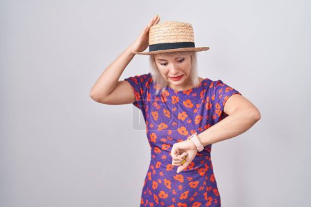 Téléchargez les photos : Jeune femme caucasienne portant des fleurs robe et chapeau d'été en regardant l'heure de la montre inquiet, peur de se tard - en image libre de droit