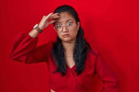 Photo for Asian young woman standing over red background worried and stressed about a problem with hand on forehead, nervous and anxious for crisis - Royalty Free Image