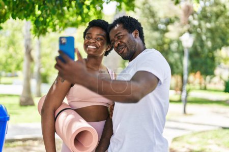 Foto de Africano americano hombre y mujer pareja celebración yoga mat haciendo selfie por el teléfono inteligente en parque - Imagen libre de derechos