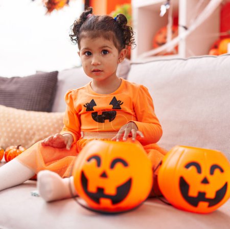 Photo for Adorable hispanic girl having pumpkin costume sitting on sofa at home - Royalty Free Image