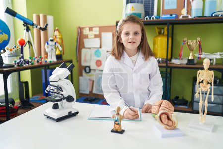Photo for Adorable blonde girl student writing notes at laboratory classroom - Royalty Free Image