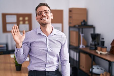 Foto de Joven hombre hispano en la oficina renunciando a decir hola feliz y sonriente, gesto de bienvenida amistoso - Imagen libre de derechos