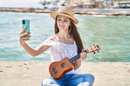 Téléchargez les photos : Adorable girl tourist make selfie by the smartphone playing ukulele at seaside - en image libre de droit