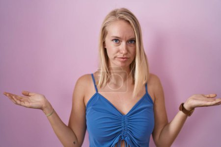 Téléchargez les photos : Young caucasian woman standing over pink background clueless and confused with open arms, no idea concept. - en image libre de droit