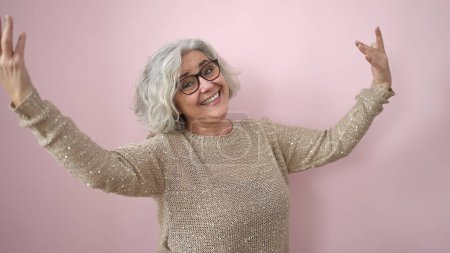 Téléchargez les photos : Middle age woman with grey hair smiling and dancing over isolated pink background - en image libre de droit