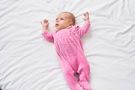 Téléchargez les photos : Adorable bébé hispanique couché sur le lit avec une expression détendue dans la chambre - en image libre de droit