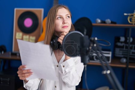 Photo for Young caucasian woman artist reading song with doubt expression at music studio - Royalty Free Image