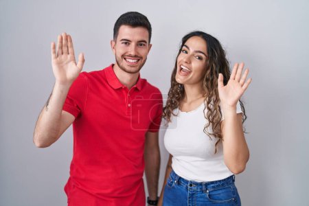 Téléchargez les photos : Jeune couple hispanique debout sur fond isolé renonçant à dire bonjour heureux et souriant, geste de bienvenue amical - en image libre de droit