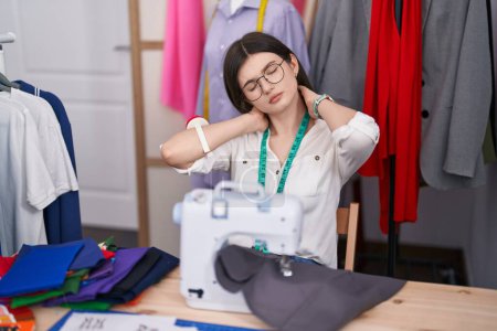 Téléchargez les photos : Jeune couturière caucasienne stressée à l'aide d'une machine à coudre au magasin de tailleur - en image libre de droit