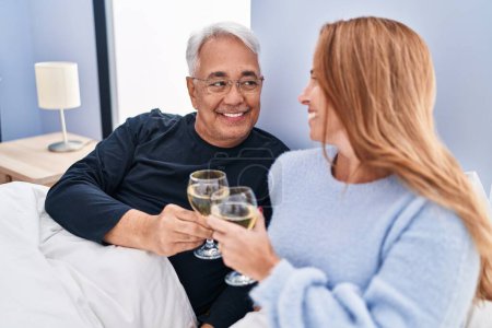 Téléchargez les photos : Couple homme / femme d'âge moyen buvant du vin couché sur le lit dans la chambre - en image libre de droit