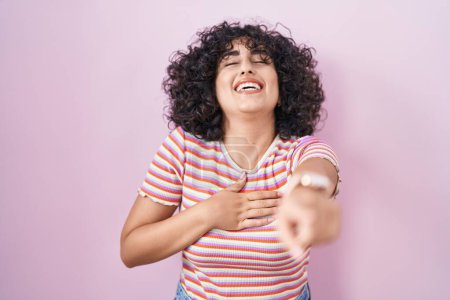 Photo for Young middle east woman standing over pink background laughing at you, pointing finger to the camera with hand over body, shame expression - Royalty Free Image