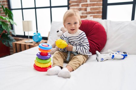 Photo for Adorable caucasian boy playing with hoops game holding duck toy sitting on bed at bedroom - Royalty Free Image