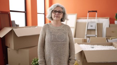 Foto de Mujer de mediana edad con el pelo gris de pie con expresión relajada en el nuevo hogar - Imagen libre de derechos