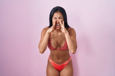 Foto de Mujer hispana con bikini gritando furiosa con las manos sobre la boca - Imagen libre de derechos