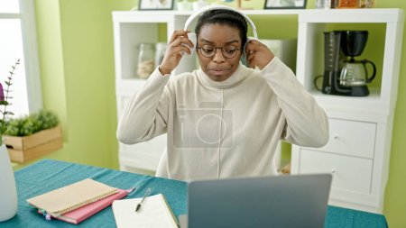 Photo for African american woman using laptop and headphones studying on table at dinning room - Royalty Free Image
