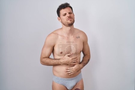 Photo for Young hispanic man standing shirtless wearing underware with hand on stomach because indigestion, painful illness feeling unwell. ache concept. - Royalty Free Image