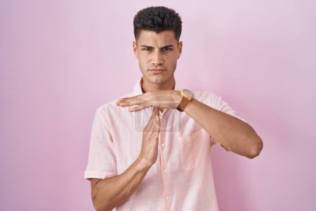 Foto de Young hispanic man standing over pink background doing time out gesture with hands, frustrated and serious face - Imagen libre de derechos