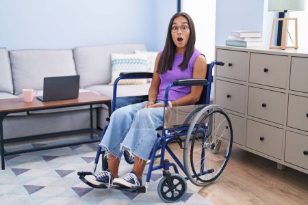 Photo for Young hispanic woman sitting on wheelchair at home afraid and shocked with surprise expression, fear and excited face. - Royalty Free Image