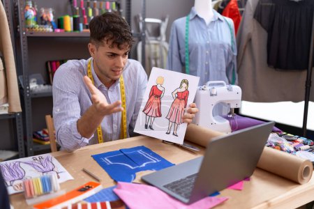 Foto de Young hispanic man tailor having video call showing clothing design at atelier - Imagen libre de derechos