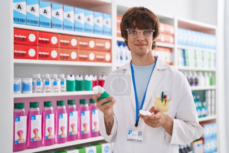 Foto de Joven farmacéutico hombre rubio sosteniendo la botella de pasta de dientes en la farmacia - Imagen libre de derechos
