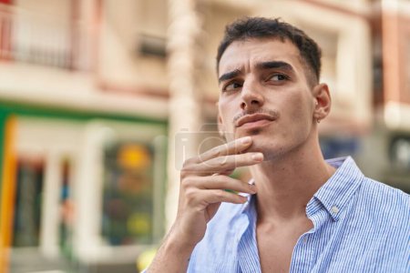 Téléchargez les photos : Jeune homme hispanique debout avec l'expression du doute dans la rue - en image libre de droit