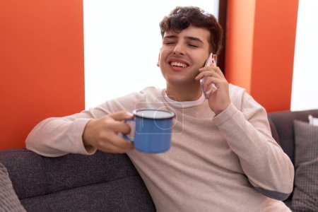 Téléchargez les photos : Homme non binaire parlant sur smartphone boire du café à la maison - en image libre de droit