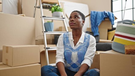 Téléchargez les photos : Femme afro-américaine assise sur le sol avec une expression détendue à la nouvelle maison - en image libre de droit