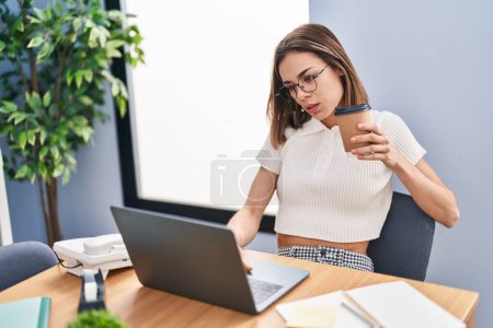 Téléchargez les photos : Jeune belle hispanique femme travailleur d'affaires en utilisant un ordinateur portable boire du café au bureau - en image libre de droit