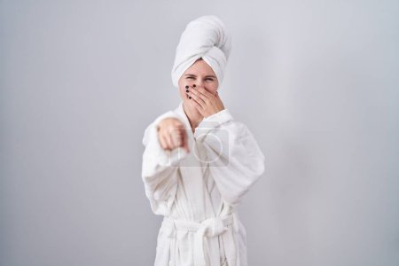 Photo for Blonde caucasian woman wearing bathrobe laughing at you, pointing finger to the camera with hand over mouth, shame expression - Royalty Free Image