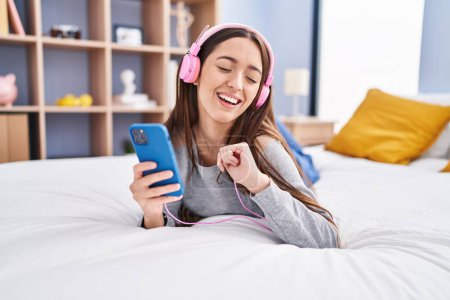 Téléchargez les photos : Jeune belle femme hispanique dansant et écoutant de la musique allongée sur le lit dans la chambre - en image libre de droit
