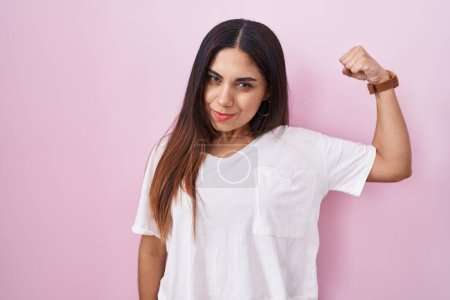 Foto de Mujer árabe joven de pie sobre fondo rosa fuerte persona que muestra el músculo del brazo, confiado y orgulloso de poder - Imagen libre de derechos