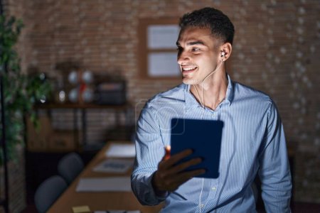 Photo for Handsome hispanic man working at the office at night looking away to side with smile on face, natural expression. laughing confident. - Royalty Free Image