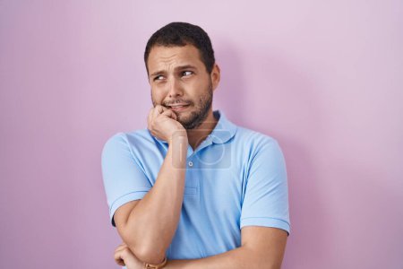 Photo for Hispanic man standing over pink background looking stressed and nervous with hands on mouth biting nails. anxiety problem. - Royalty Free Image