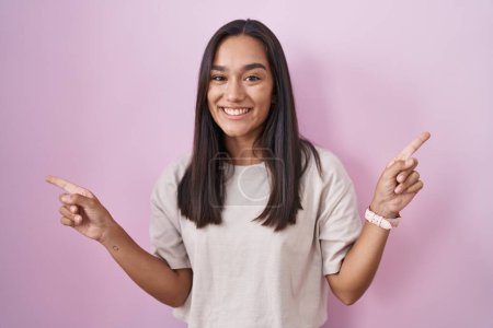 Photo for Young hispanic woman standing over pink background smiling confident pointing with fingers to different directions. copy space for advertisement - Royalty Free Image
