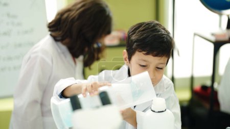 Téléchargez les photos : Adorable garçon et fille étudiant versant du liquide sur un tube à essai dans une salle de classe de laboratoire - en image libre de droit