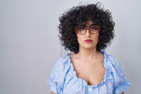 Photo for Young brunette woman with curly hair wearing glasses over isolated background relaxed with serious expression on face. simple and natural looking at the camera. - Royalty Free Image