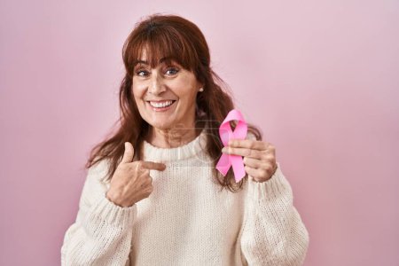 Photo for Middle age hispanic woman holding pink cancer ribbon pointing finger to one self smiling happy and proud - Royalty Free Image