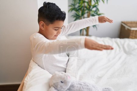 Téléchargez les photos : Adorable garçon hispanique somnambule assis sur le lit dans la chambre - en image libre de droit