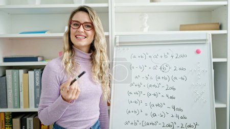 Foto de Joven mujer rubia profesora enseñando matemáticas lección en el aula - Imagen libre de derechos