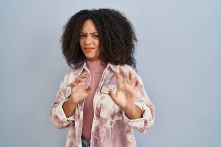 Photo for Young african american woman standing over blue background disgusted expression, displeased and fearful doing disgust face because aversion reaction. with hands raised - Royalty Free Image