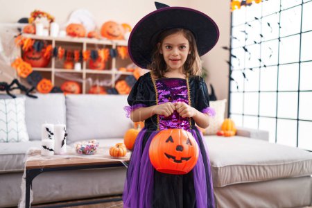 Foto de Adorable chica hispana teniendo fiesta de halloween sosteniendo canasta de calabaza en casa - Imagen libre de derechos