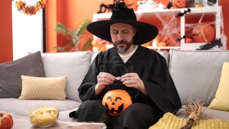Foto de Joven calvo con traje de mago sosteniendo dulce de calabaza cesta de halloween en casa - Imagen libre de derechos