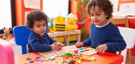 Foto de Adorables chicos afroamericanos jugando con matemáticas juego de puzzle sentado en la mesa en el jardín de infantes - Imagen libre de derechos